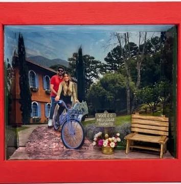 Quadro 3D em caixa vermelha com a foto de um casal de bicicleta, casa, jardim, banco e a placa Você é o meu lugar favorito